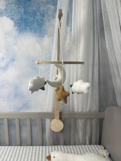 a baby crib with a stuffed animal hanging from it's side and clouds on the wall