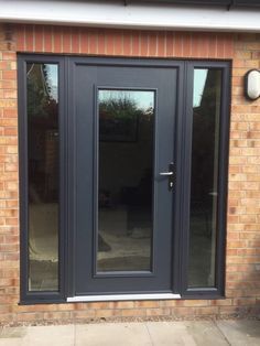 a black double door with glass on the side of a brick wall and grey trim