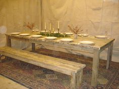 a wooden table with plates and candles on it in front of a white curtained wall