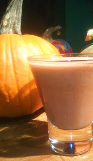 a glass filled with liquid sitting on top of a wooden table next to pumpkins