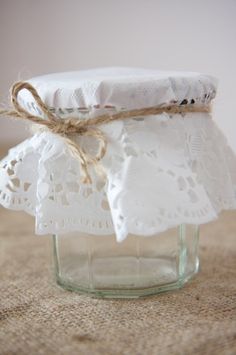 a glass jar filled with white doily and twine on top of a table