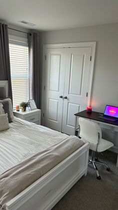 a white bed sitting next to a window with curtains on the windowsill and a desk in front of it