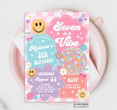 a pink plate with a card on it that says seven is a vibe, and features smiley faces