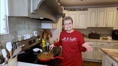 an older woman standing in a kitchen with her hands out to the side while holding a frying pan full of food