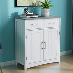 a white cabinet with two drawers and a potted plant on top in a blue room