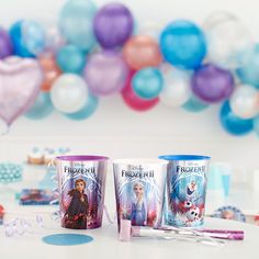 three frozen princess mugs sitting on top of a table next to balloons and confetti