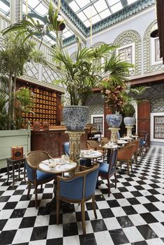 an indoor dining area with black and white checkered flooring, potted palm trees, and blue chairs