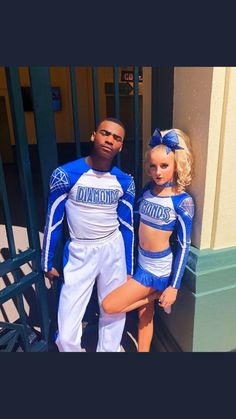 a man and woman dressed in cheerleader outfits standing next to each other near a fence