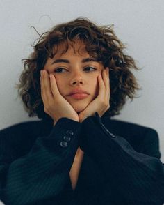 a woman with her hands on her face, sitting in front of a white wall