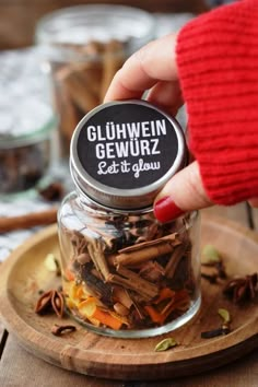 a person holding a jar filled with spices on top of a wooden tray next to other items