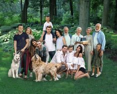 a group of people and their dogs posing for a photo in the grass with trees behind them