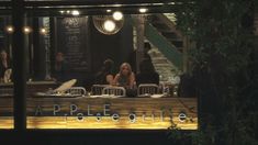 people are sitting at tables in front of the restaurant's window, with lights on