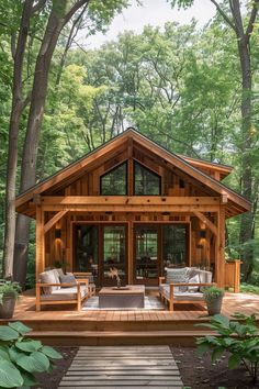 a small wooden cabin in the woods with seating and wood flooring, surrounded by trees