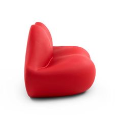 a red heart shaped chair sitting on top of a white floor next to a wall