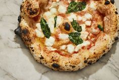 a pizza with cheese, spinach and other toppings sitting on a marble surface