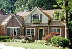 a brick house with green shutters and white trim on the front door is surrounded by lush greenery