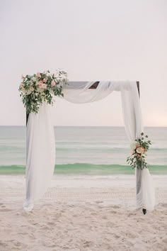 an outdoor ceremony setup on the beach with white draping and flowers in front of the ocean