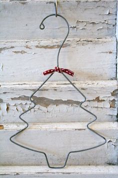 a metal wire christmas tree decoration hanging on a white painted wooden wall with red ribbon