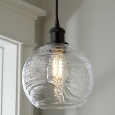 a clear glass light fixture hanging from a ceiling in a room with white walls and trimmings