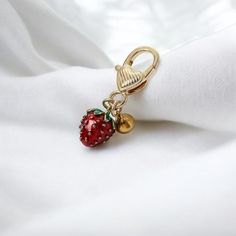 a red strawberry charm sitting on top of a white cloth next to a gold bell