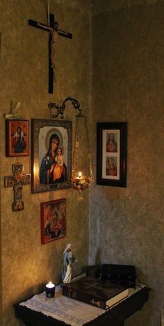 a cross hanging on the wall next to a table with candles and pictures above it