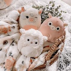 three stuffed animals sitting in a basket on a blanket next to some plants and flowers