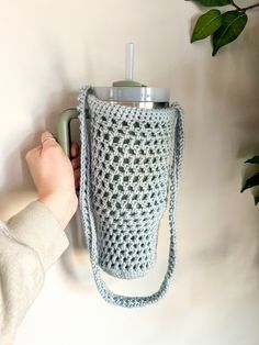 a person is holding onto a crocheted cup holder with a water bottle in it