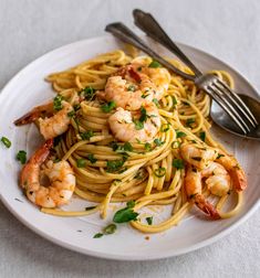 pasta with shrimp and parsley on a white plate next to a fork, knife and spoon