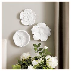 three white flowers sitting on top of a table next to a vase filled with flowers