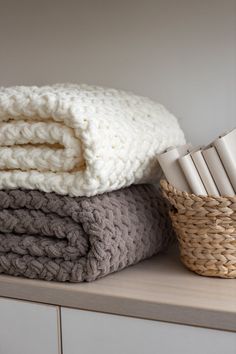 stack of folded blankets on top of a shelf next to a basket and napkins