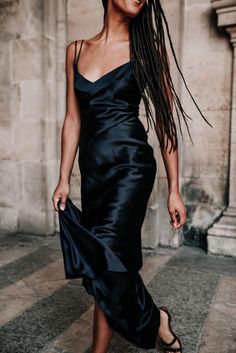 a woman with dreadlocks is walking down the street wearing a black dress and sandals