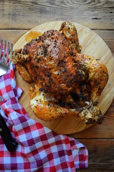 a whole chicken sitting on top of a wooden plate next to a knife and fork