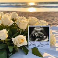 a bouquet of white roses sitting on top of a table next to a card with an image of a baby