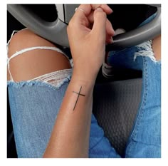 a woman with a cross tattoo on her arm sitting in the drivers seat of a car