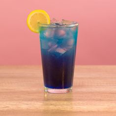 a blue drink with ice and lemon wedges on the rim, sitting on a wooden table