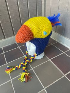 a crocheted bird hat with colorful feathers on it's head and tail