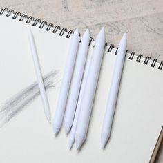 three white pens sitting next to each other on top of a notepad with pencils