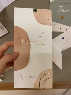 a person holding up a card with the word miou in gold foil on it