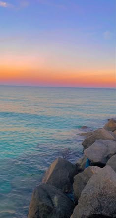 there is a bench sitting on the rocks by the water at sunset or sunrise time