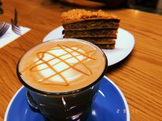 a blue plate topped with a piece of cake next to a cup of cappuccino