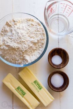 ingredients needed to make cheesecakes laid out on a white wooden table with measuring cups