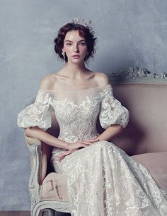 a woman sitting on top of a couch wearing a white dress with an off the shoulder design