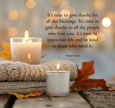 a white candle sitting on top of a wooden table next to some blankets and leaves