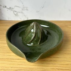 a green ceramic bowl with a leaf decoration on the top and bottom, sitting on a wooden surface