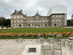 there are many chairs and tables in front of a large building with flowers on the lawn