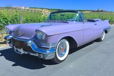 an old purple car parked on the side of the road in front of a vineyard