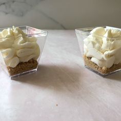 two desserts with banana slices and whipped cream in small glass dishes on a table