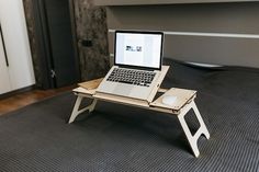 an open laptop computer sitting on top of a wooden table with a tray underneath it