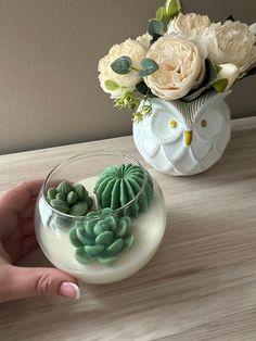 a hand is holding a small bowl with succulents in it next to a flower arrangement