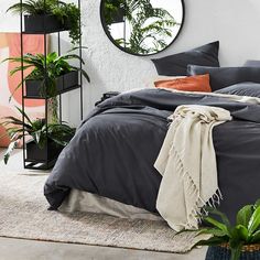 a bed in a bedroom next to a mirror and potted plants